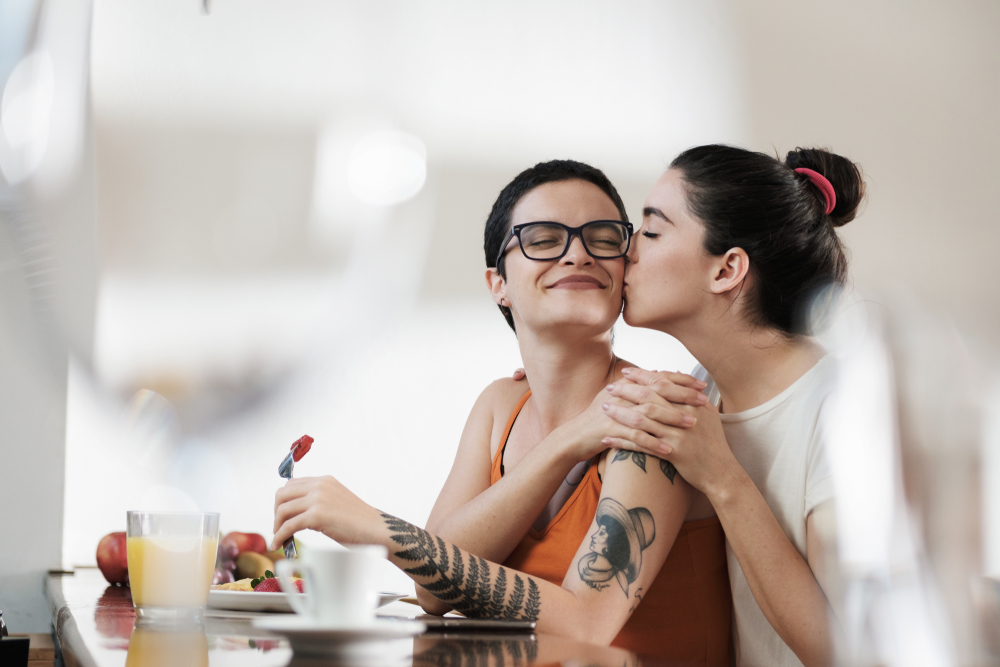 A lesbian couple has breakfast together, they are holding hands and smiling affectionately