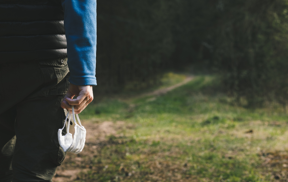 Un uomo di spalle davanti ad un bosco, con in mano una mascherina chirurgica