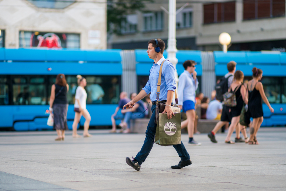 Un giovane uomo cammina in centro a Zagabria con una borsa e le cuffie - © Ivica Drusany