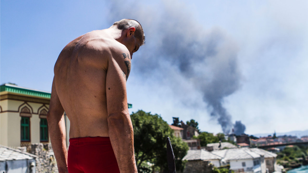 A man looks down from the bridge, ready to dive into the Neretva river in Mostar (screenshot from the film "I tuffatori" by Daniele Babbo)