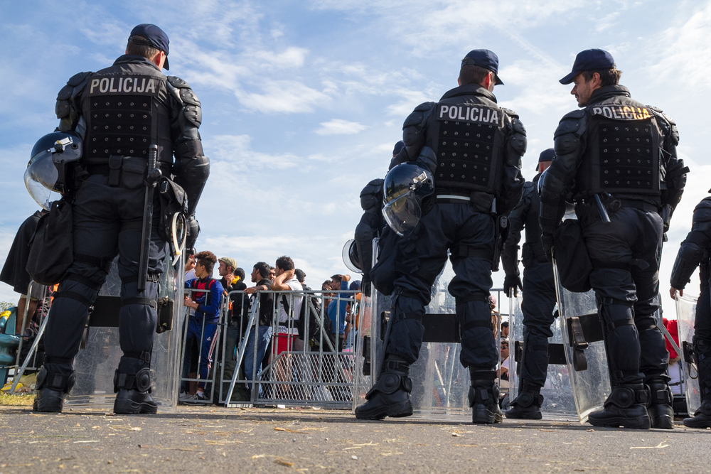 Some Croatian policemen in shields guard a fence that divides them from the mass of migrants on the border between Croatia and Bosnia