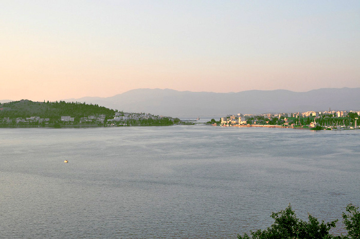 Lo stretto dell'Euripo con il famoso ponte. Sulla destra, il centro di Calcide, alle cui spalle si levano i grandi monti dell'isola Eubea. A sinistra, la Grecia continentale