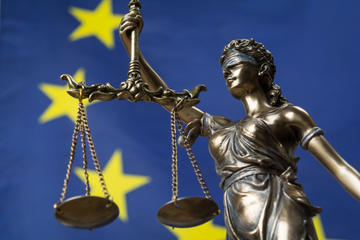 Statue of the goddess of justice against an European flag. Credits: Respiro via Shutterstock