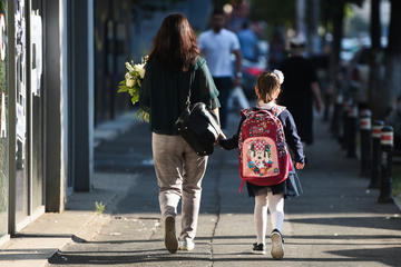 A mother, photographed from behind, accompanies her daughter to school