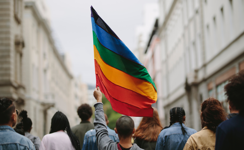 Durante un Pride, persone che camminano di spalle e alzano una bandiera arcobaleno © Jacob Lund/Shutterstock Durante un Pride, persone che camminano di spalle e alzano una bandiera arcobaleno © Jacob Lund/Shutterstock