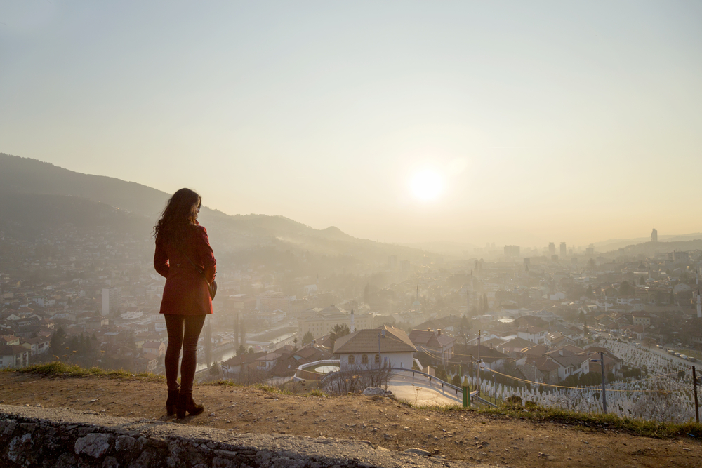 Una donna guarda la città di Sarajevo dall'alto al tramonto © novak.elcic/Shutterstock
