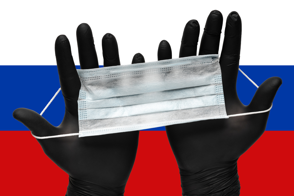 Due mani in guanti neri tengono una maschera chirurgica con la bandiera russa sullo sfondo