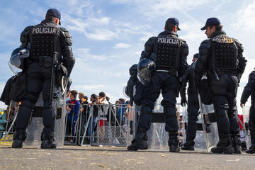 Alcuni poliziotti croati in tenuta anti sommossa stazionano davanti ad un transenna che li divide dalla massa di migranti al confine tra Croazia e Bosnia