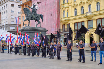 Zagreb, Croatia, June 23, 2019 : Right wing political rally in city main square, featuring man dressed in black waving Croatian, Black and Anti EU flags (© meandering images/Shutterstock)