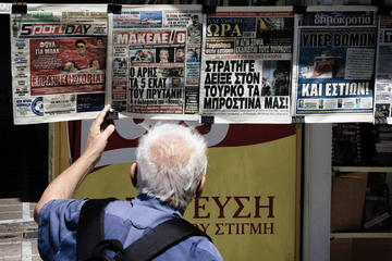 An elderly man reads the front pages of newspapers at a newsstand in Athens © Theastock/Shutterstock