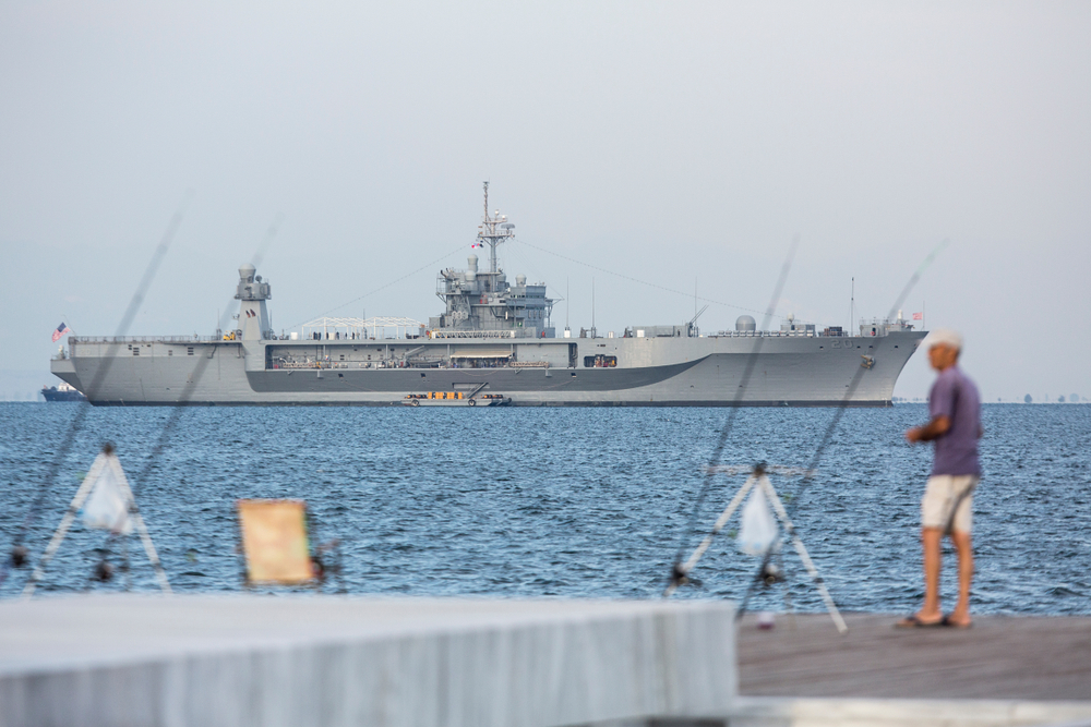 Thessaloniki, Greece - September 11, 2018. A man fishes at the seafront of the city with the USS Mount Whitney at the background - Giannis Papanikos