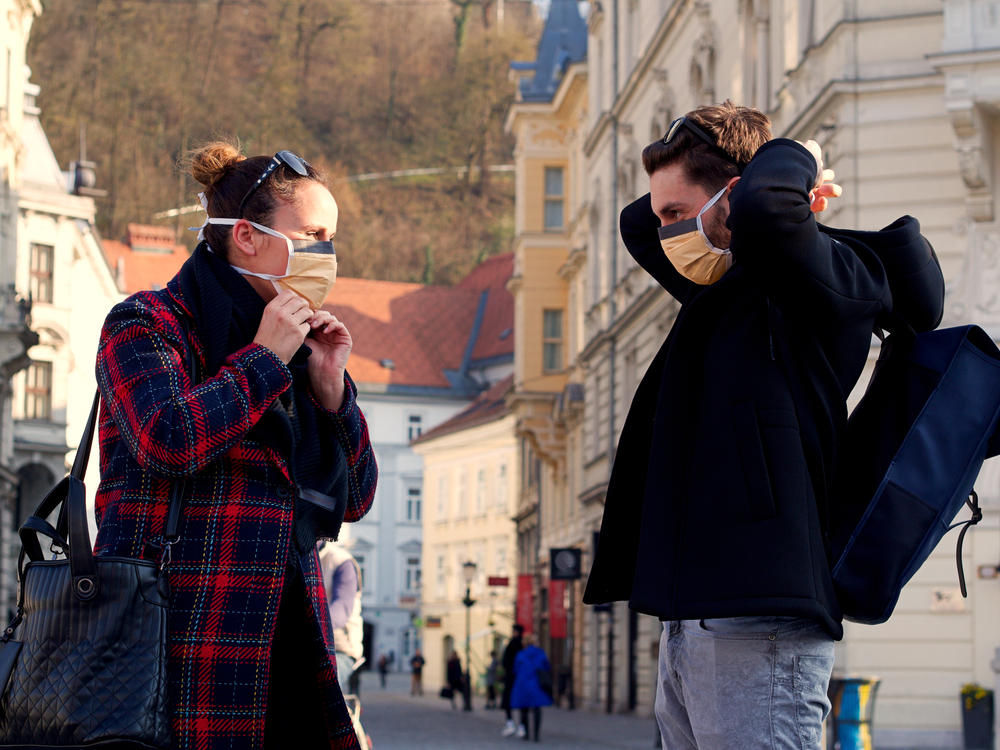 Young couple putting on a face protection face mask in the city center of Ljubiana - © Gasper Grubelnik/Shutterstock