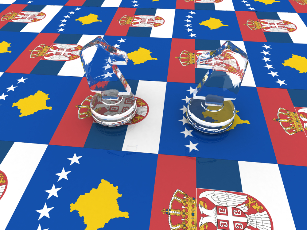 Una scacchiera fatta con le bandiere di Serbia e Kosovo, i due cavalli dei rispettivi gocatori stanno uno di fronte all'altro