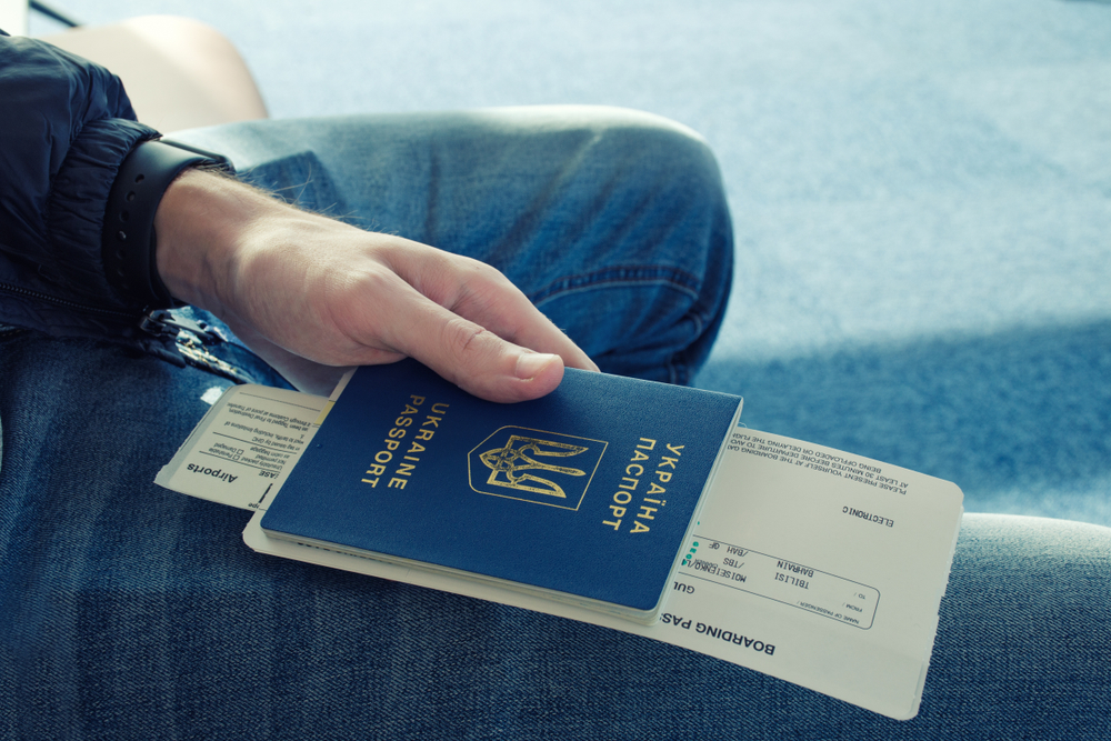 Un uomo in jeans tiene in mano un passaporto ucraino e dei biglietti dell'aereo © Lina Mo/Shutterstock