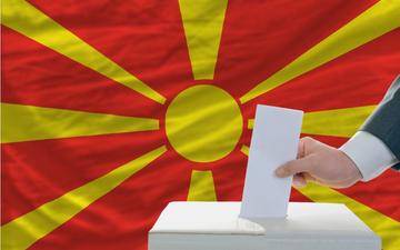 Man putting a ballot in a box during elections in North Macedonia in front of the state's flag -  © vepar5/Shutterstock 