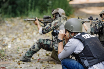 Un reporter fotografa una scena di guerra insieme con dei militari © PRESSLAB/Shutterstock