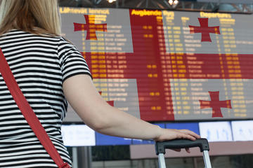 Donna guarda un tabellone dei voli in aeroporto, sullo sfondo bandiera della Georgia © Artmim/Shutterstock