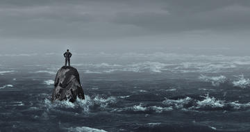 Un uomo solo sta in pidi su uno scoglio nel bel mezzo di un mare in burrasca © Lightspring/Shutterstock