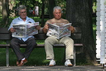 Two men reading a newspaper on a bench in Bucharest 