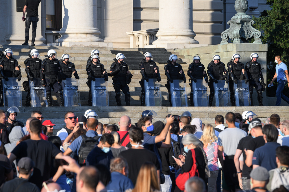 Gruppo di persone protesta davanti ad un cordone di polizia in tenuta antisommossa (© Bobica10/Shutterstock)