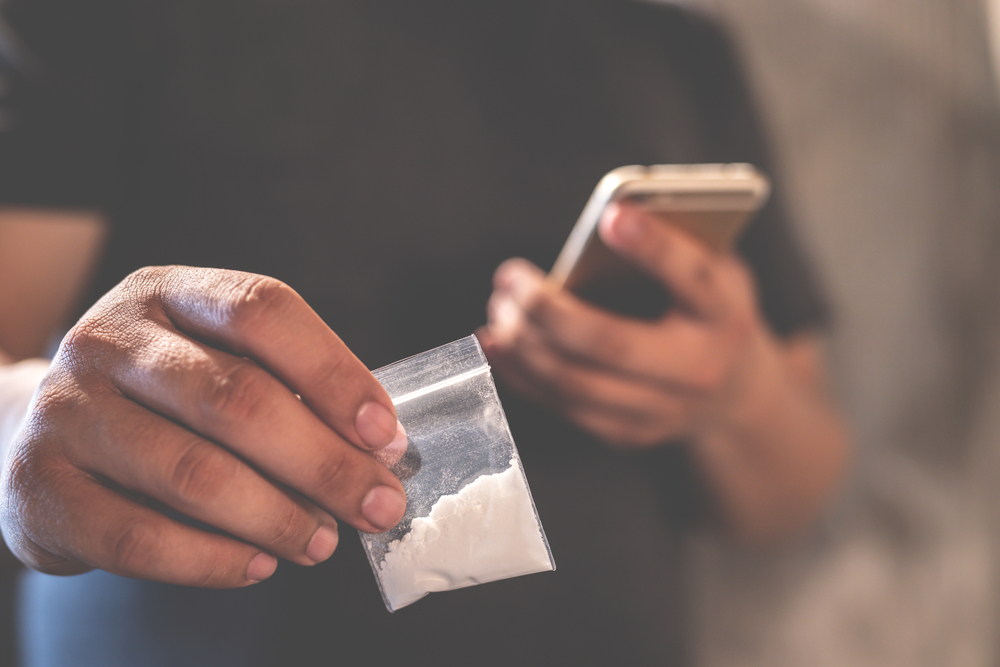hands of a person holding a smartphone and a plastic bag with white powder hands of a person holding a smartphone and a plastic bag with white powder