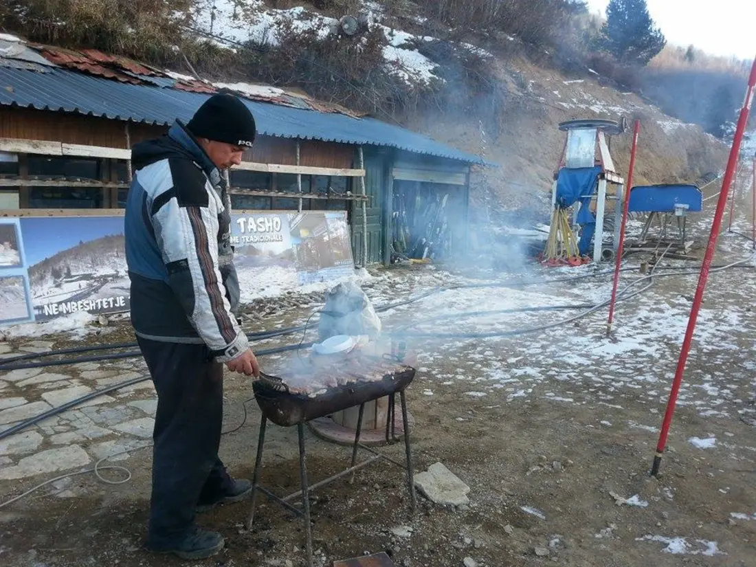 Barbecue in the mountains- Local man welcoming visitors with regional delicacies: qebap (kebap) and home-made rakija – Photo: Mary Drosopoulos Barbecue in the mountains- Local man welcoming visitors with regional delicacies: qebap (kebap) and home-made rakija - Photo: Mary Drosopoulos